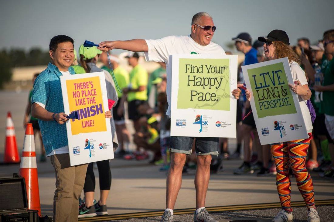 Volunteers hold motivational signs and cheer for runners at the 5K on the Runway.