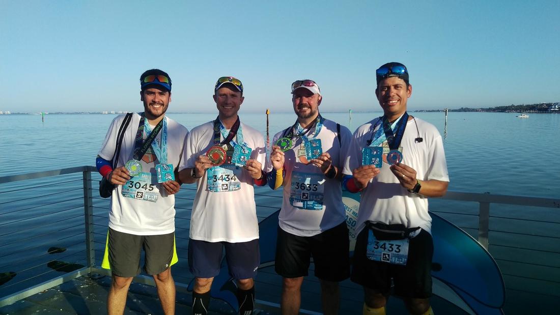 Runners pose with medals in front of Sarasota Bay, FL.