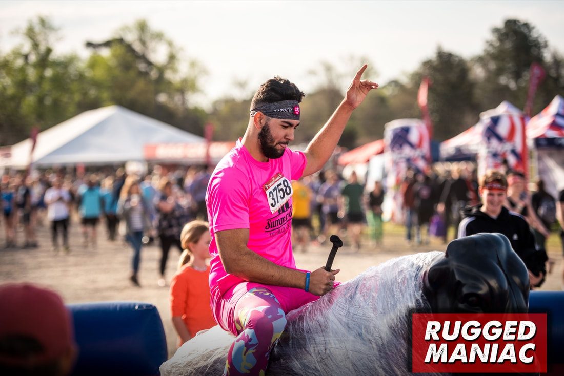 Guy riding mechanical bull at Rugged Maniac festival.