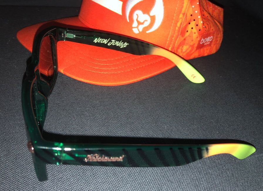 Closeup of Knockaround Neon Jungle sunglasses in front of an orange BibRave trucker hat.