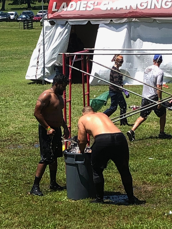Rugged Maniac racers wash off in a garbage can filled with water.