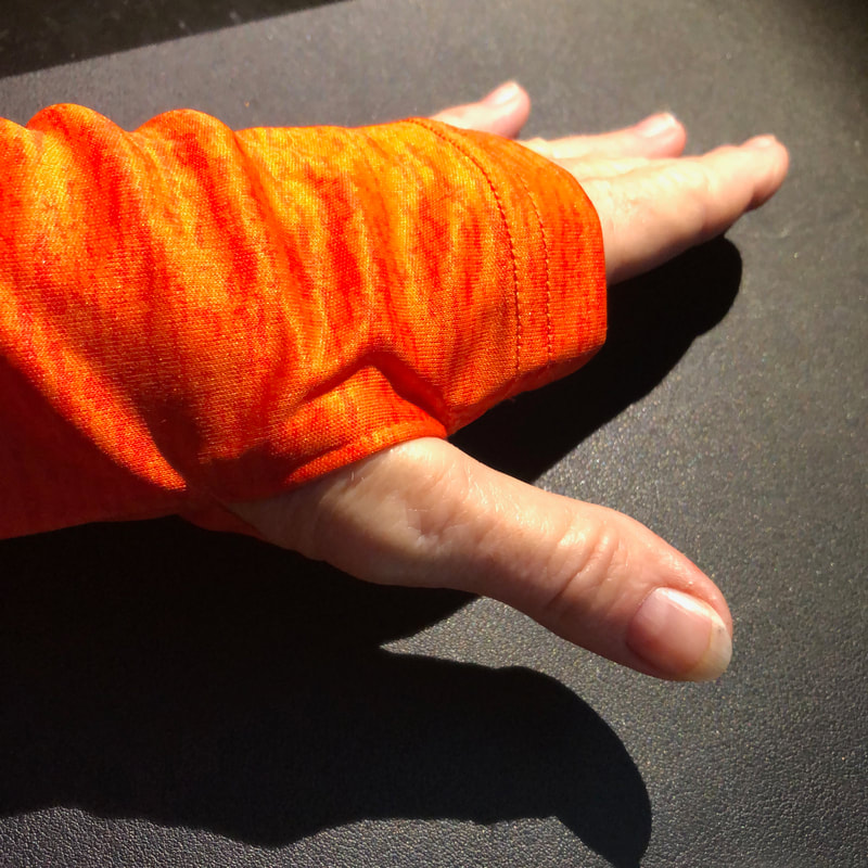 Photo of hand in the orange long sleeve pullover, using the thumbholes in the sleeves.