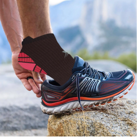 Image of man putting his foot into a running shoe while wearing compression socks.