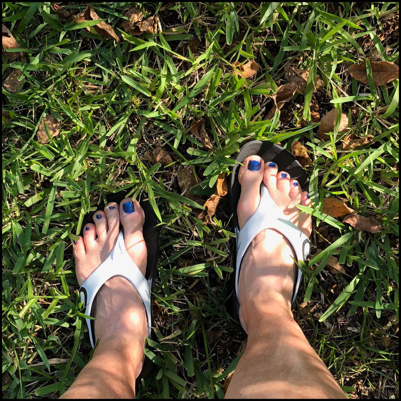 Feet in Oofos sandals in green grass.